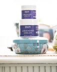 Two jars of lavender cream on a surface with a blurred background