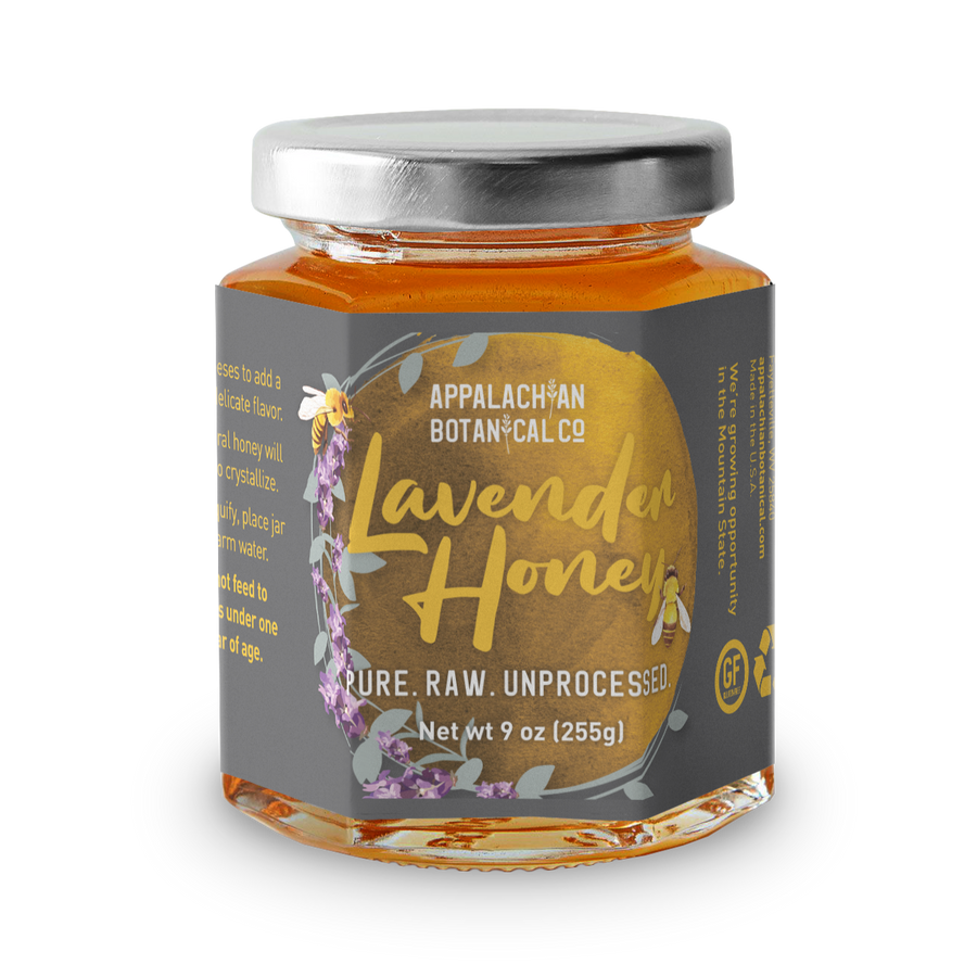 Clear glass jar filled with honey. The jar has a silver, metal cap and a gray label. The label has a golden circle that is bordered by a lavender stalk and a bee on the left side. Inside the circle, the text "Appalachian Botanical Co ; Lavender Honey ; Pure. Raw. Unprocessed ; Net wt 9 oz [255g]" is printed. The text "Lavender Honey" is yellow with the image of a bee next to the 'y', while the rest of the text is white. Along the sides of the label, there is text printed in yellow that is unreadable.